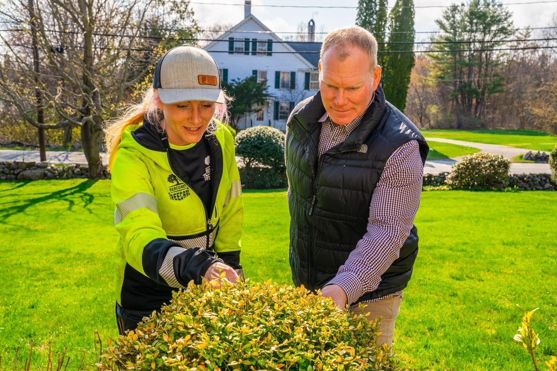plant health technician inspecting the health of a shrub with a client